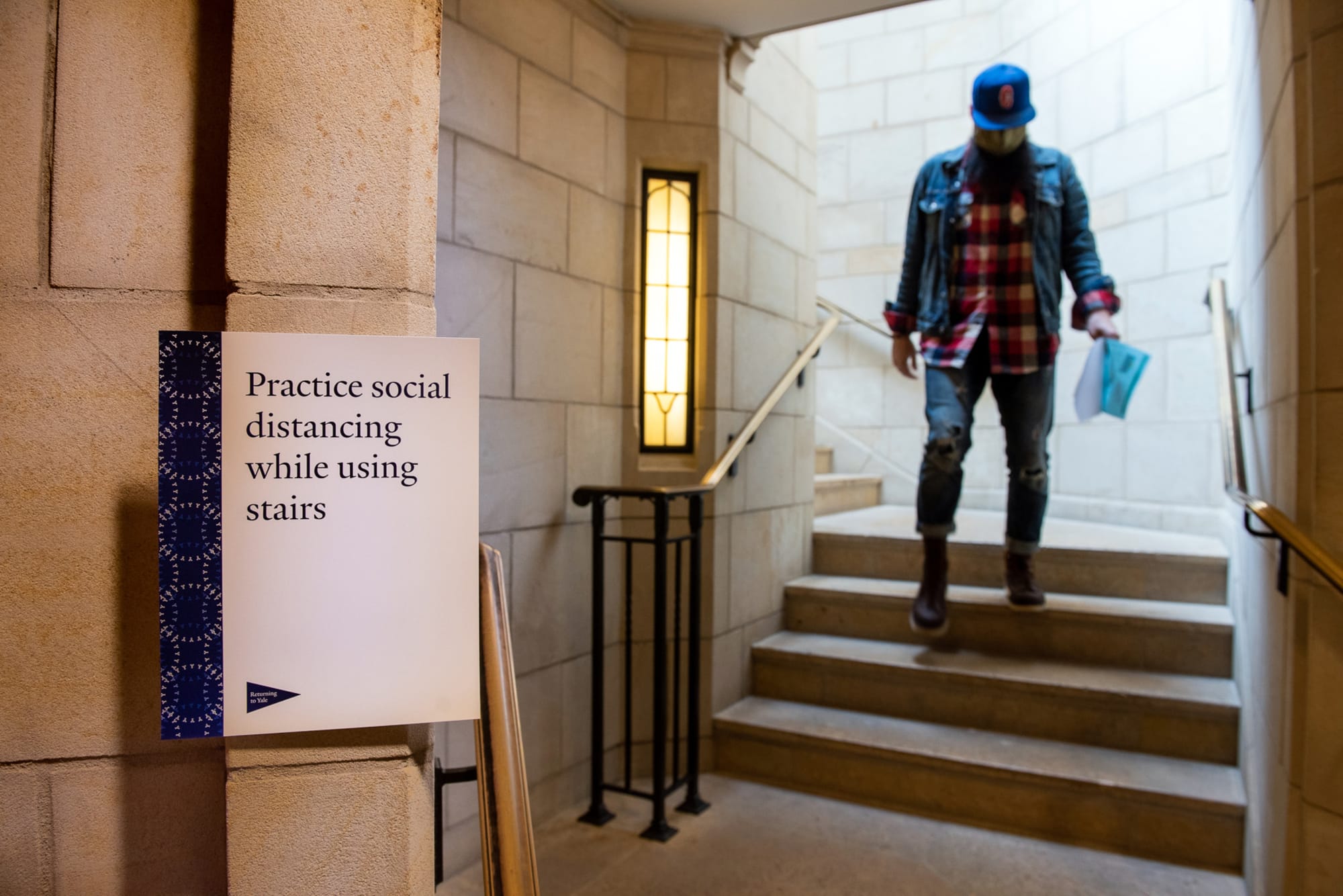 Man descending stair from Sterling nave with physical distancing signage in foreground 