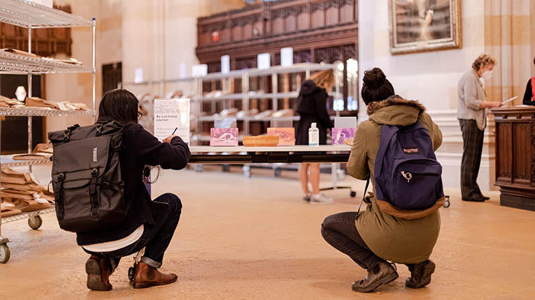 Two students writing postcards while kneeling at a desk in the Sterling nave