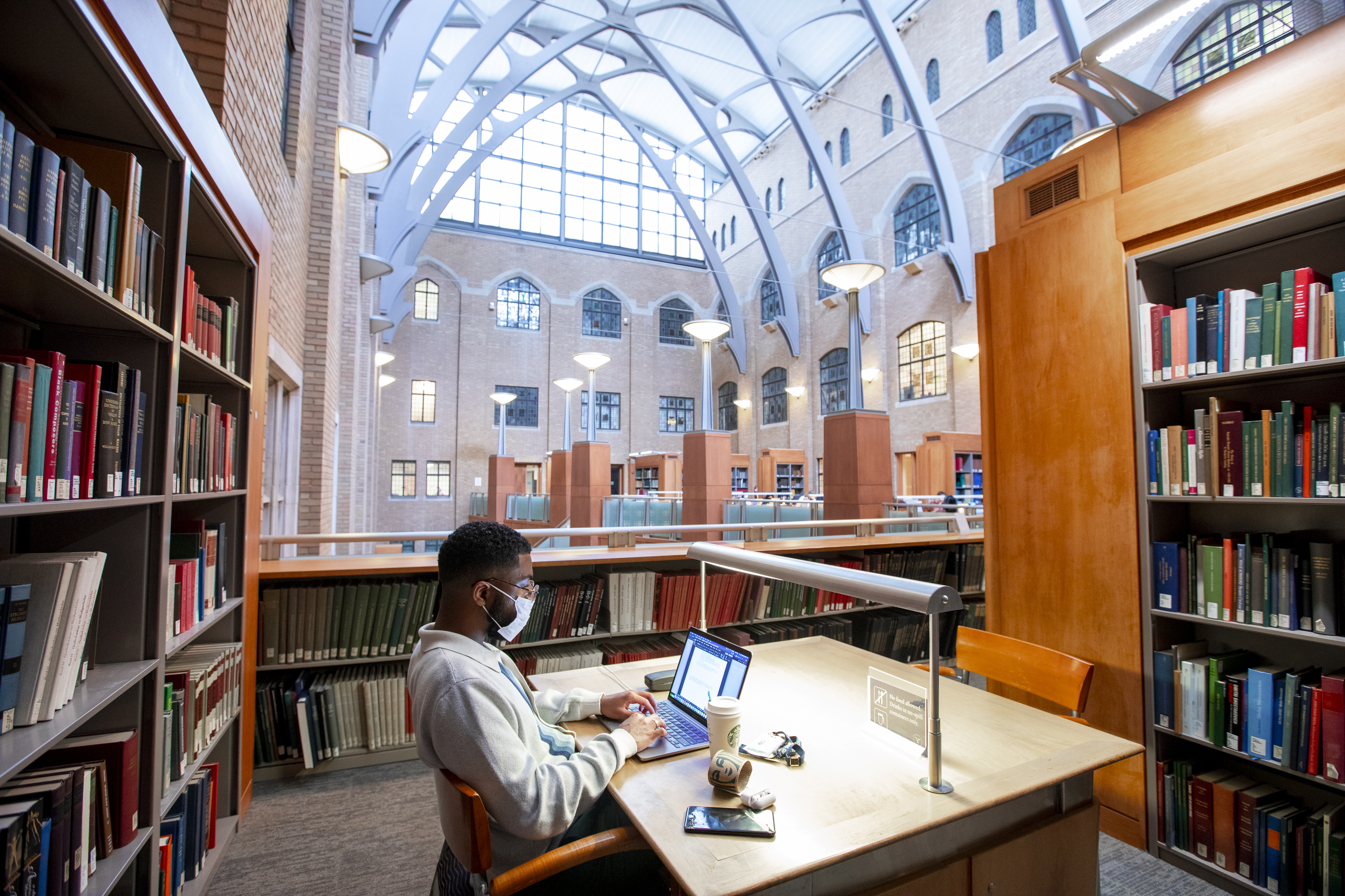student sitting at a desk studying with bookcases on either side and arched interior courtyard ceiling in the background
