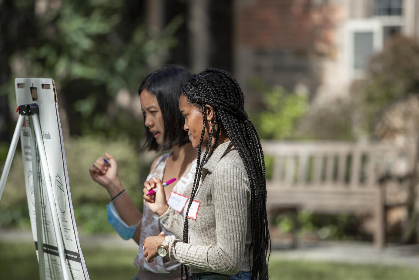 Side view of two dark haired women students collaborating in front of an easel