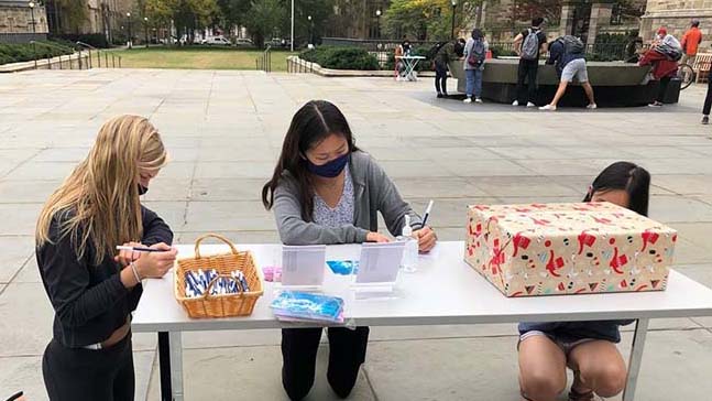 Three students writing postcarsd at a table