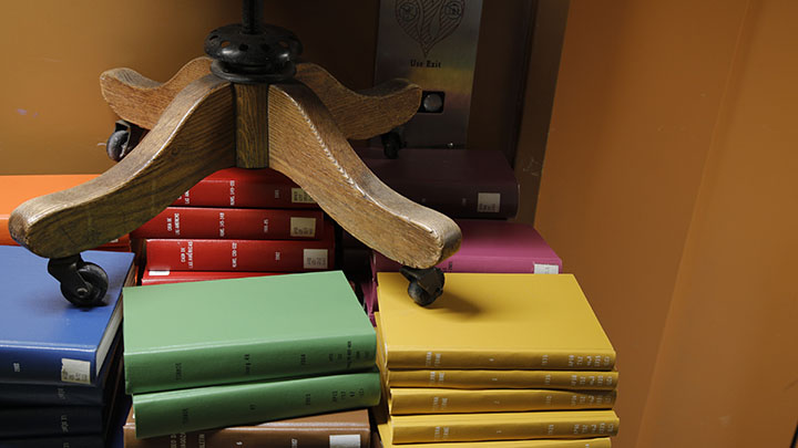 Stacks of green, blue, and yellow books with base of wooden chair on rollers on top