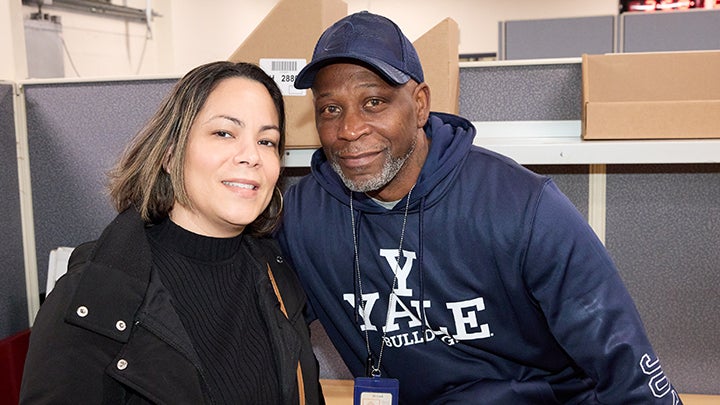 Woman with short brown hair and black shirt and jacket poses with man with blue cap and sweater with white letters that read "Y Yale Bulldogs"