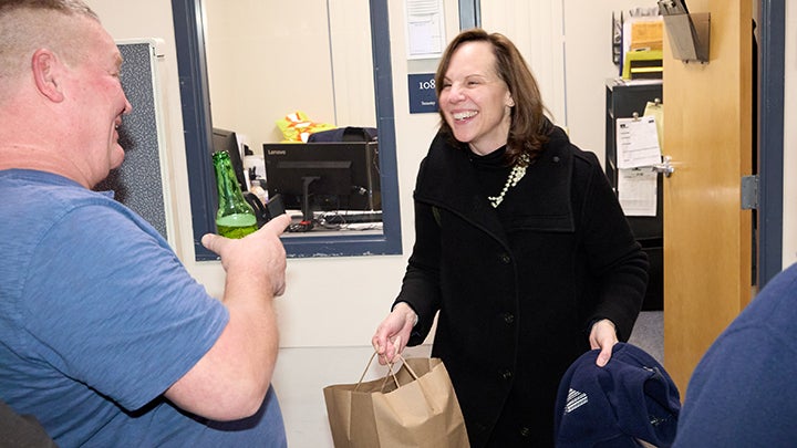 Man in blue t-shirt holding beer bottle points to woman in black coat who is laughing and holds a brown paper bag and blue fleece jacket