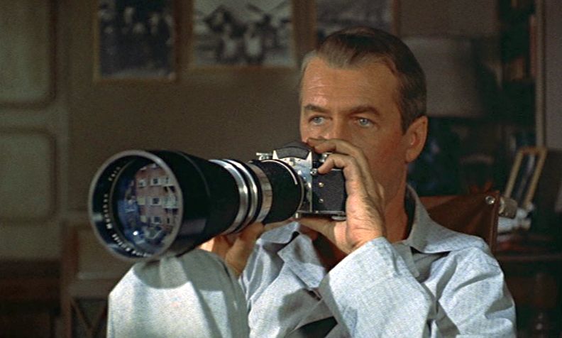 Actor Jimmy Stewart is holding up a camera with a large telephoto lens