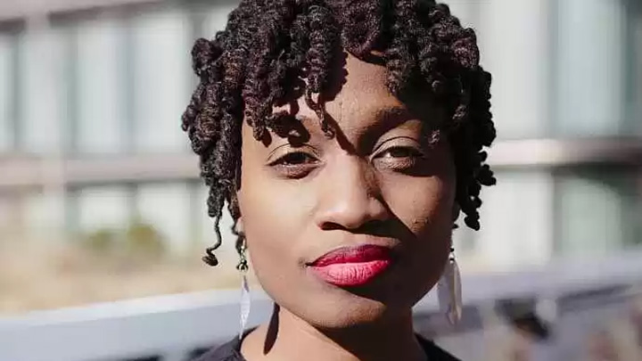 Photo of Aleshea Harris, who has curly hair and wears red lipstick, a black round-neck top, and silver dangle earrings