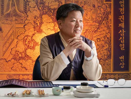 Man sitting at a desk with calligraphy brushes, inks, and bowls