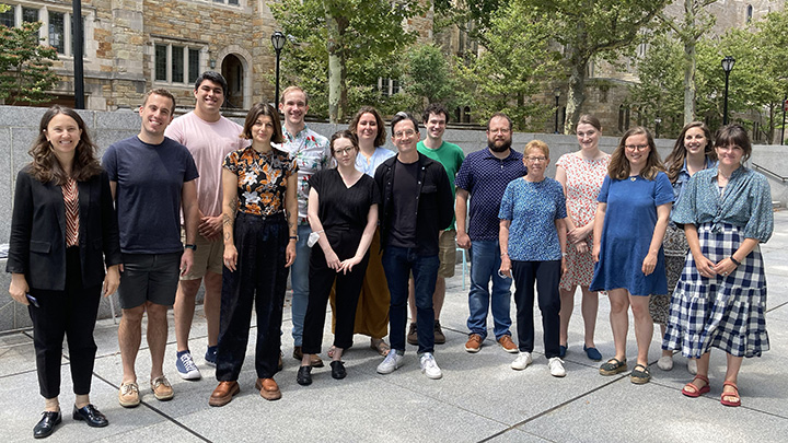 Fifteen people pose in Beinecke's granite courtyard. There are nine women and six men. Fourteen are fellows and one is a staff member.