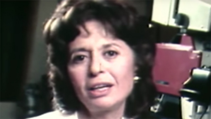 Woman with short brown hair looks at camera, in backgroud are 1970s-style television cameras.