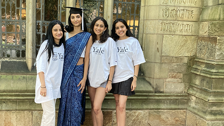 Four young women pose in Selin Courtyard. Tallest one wears graduation cap and blue and white sari, the other three all with dark hair wear tee shirts that read "Yale"