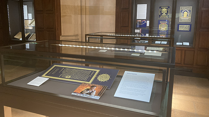 Partial view of gallery space showing two glass vitrines and one three-part wall case displaying Korean artwork in gold and dark blue