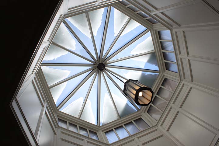 View from below of  octagonal skylight segmented into 16 triangular sections with snow on the exterior and a pendant lamp. 