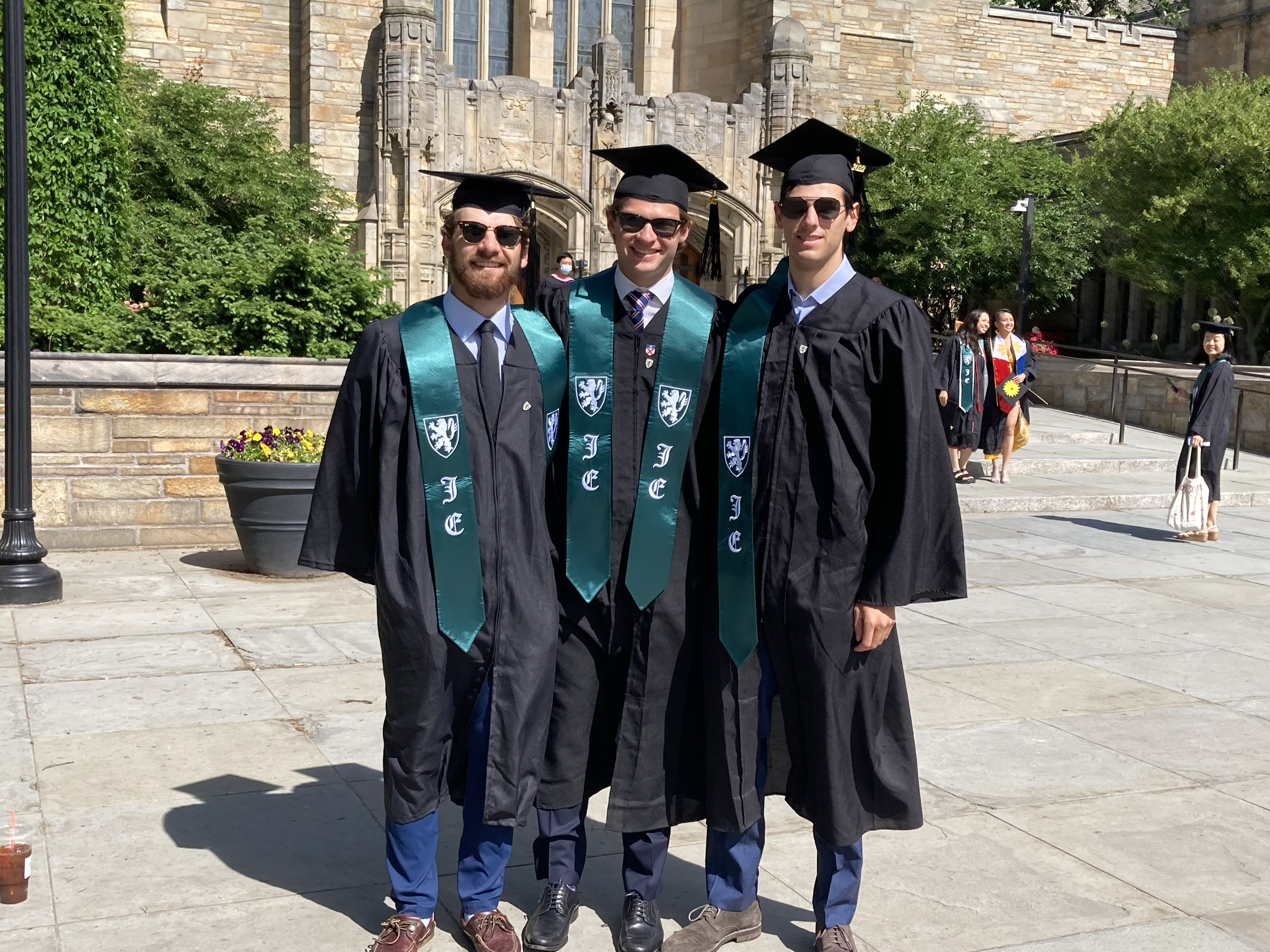 Three male graduates wearing caps, gowns, and sunglasses with green stoles with lion insignia for Jonathan Edwards College