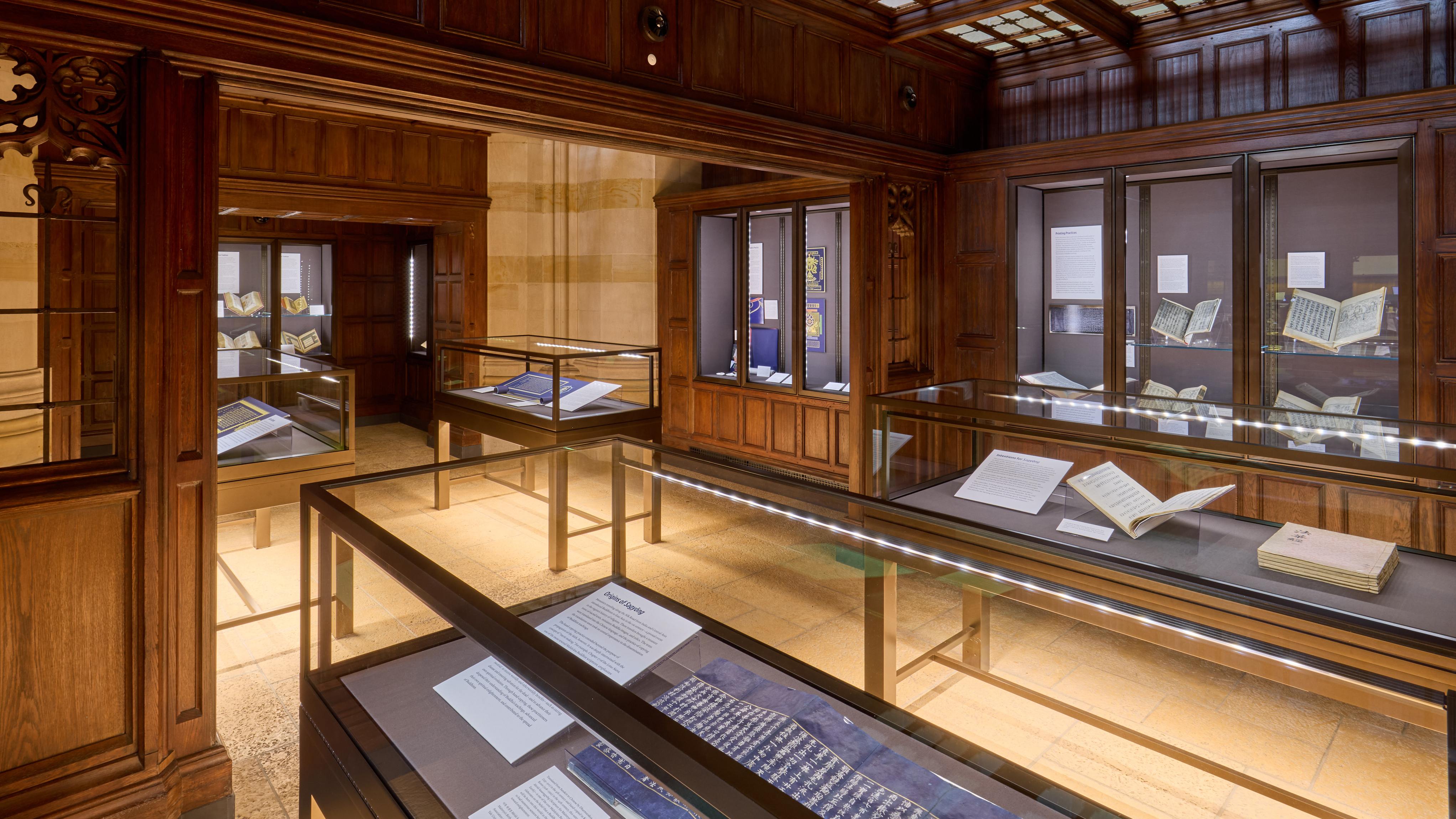 Panoramic view of gallery space with wood cabinetry, glass table and wall cases. In foreground is visible a long indigo-blue scroll with gold Korean characters