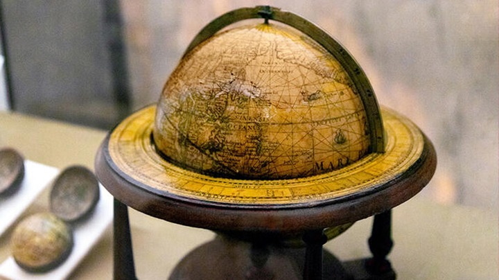 Yellowed globe, with navigation lines across its surface showing land and water, dating from circa 1621, in a wooden stand with a metal semicircular band spanning the top hemisphere