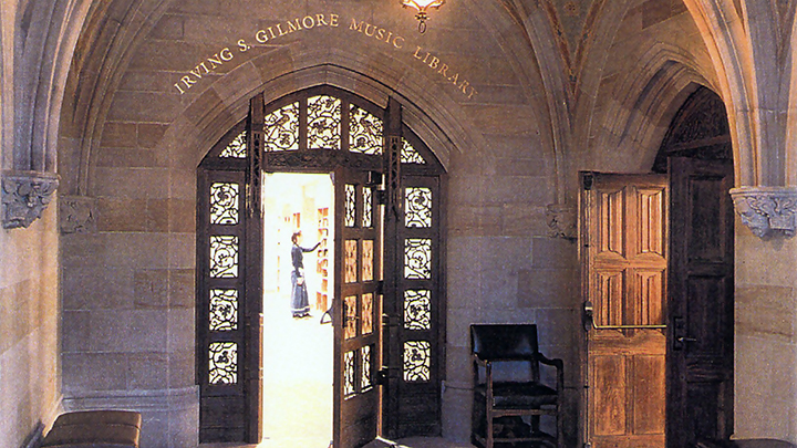 Arched doorway with leaded glass and the words "Irving S. Gilmore Music Libray" in gold letter above. Through the open doorway is a female figure in dark clothing.