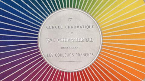 Graphic design showing a gray circle set in the middle of rectangle that has rainbow gradations of color. Words are lightly printed on the gray circle  reading 1er cercle chromatic de M. Chevreulr les couleurs franches." Diagonal white lines radiate out from the perimeter of the circle across the colored field.