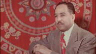 writer Langston Hughes wearing red patterned tie and brown jacket with large red, beige, and grey patterned wall hanging behind him.