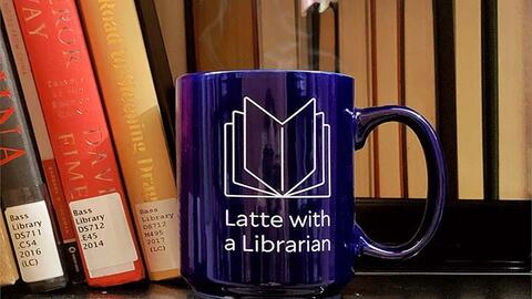 blue mug in a bookshelf, with Latte with a Librarian engraved on it