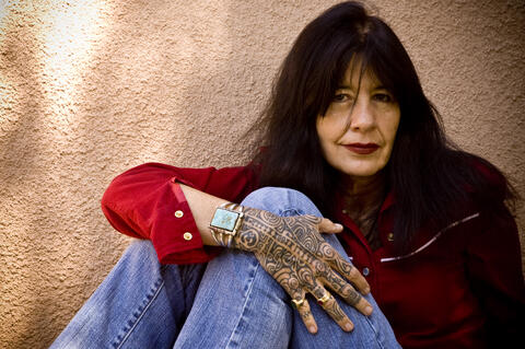 An image of a seated woman leaning on the wall showing a hand with tattoo
