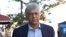 Portrait of Vijay Seshadri, who has salt-and-pepper hair, wears round wire-rimmed glasses and has a light blue collared shirt, open at the neck, and a darker blue sports jacket