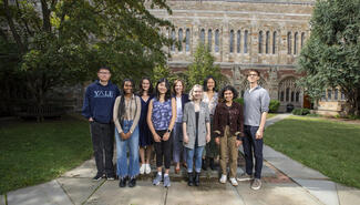 Group photo of students in a courtyard with stone and brick building in the background