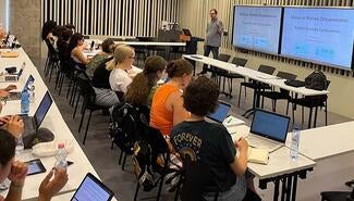 Man with glasses stands in front of wall screens that read "Diaries as Wartime Documentation." Two rows of students sit in front of him at long desks with laptops open.