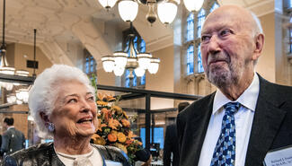 Smiling man and woman wearing name tags identifying them as Barbara Franke and Richard Franke with flowers and library reading room in the background background 