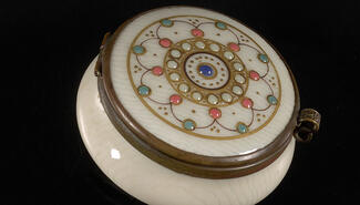 Small white round powderbox decorated with blue white and coral cloisonne, with a center circle and star shapes across the top surface