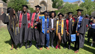 Eight graduates in caps and gowns--from Branford, Davenport, and Morse Colleges--are posing and laughing, several wearing kente cloth stoles.