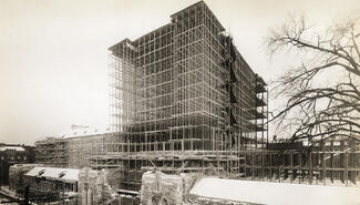 black and white photo of steel framework of seven levels of building above gothic stone bass