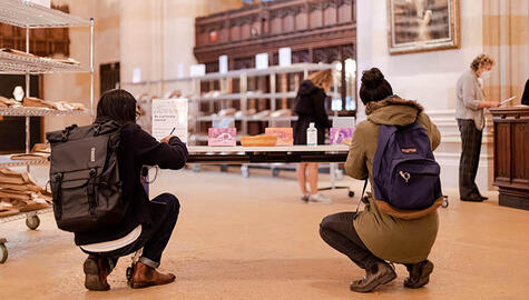 Two students writing postcards while kneeling at a desk in the Sterling nave