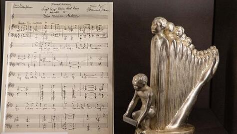 Hand-written sheet music titled "Lift Ev'ry Voice And Sing"; at right a small metal sculpture of a harp made up of standing figures with crouching boy at front