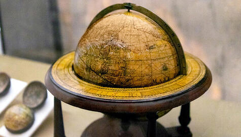 Yellowed globe, with navigation lines across its surface showing land and water, dating from circa 1621, in a wooden stand with a metal semicircular band spanning the top hemisphere