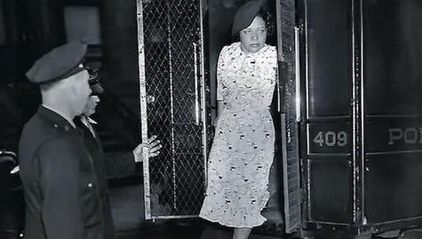 Vintage black and white image of two policemen holding open the doors of prisoner transport vehicle while a woman in a light print dress  and dark beret steps out