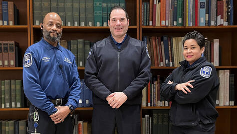From left to right: two male and one female security team members in Yale blue uniforms sending in front of Library shelves