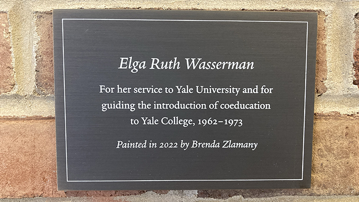 Black wall plaque with white lettering that reads "Elga Ruth Wasserman, For her service to Yale University and for guiding the introduction of coeducation to Yale College, 1962—1973, Painted in 2022 by Brenda Zlamany